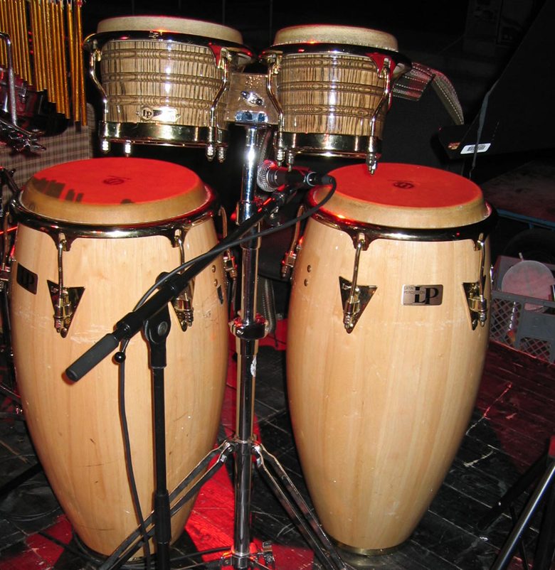 Bong&oacute;s montados en un soporte por encima de dos congas en un escenario: se aprecia que los parches del bong&oacute; son mucho m&aacute;s peque&ntilde;os que los de cualquier conga