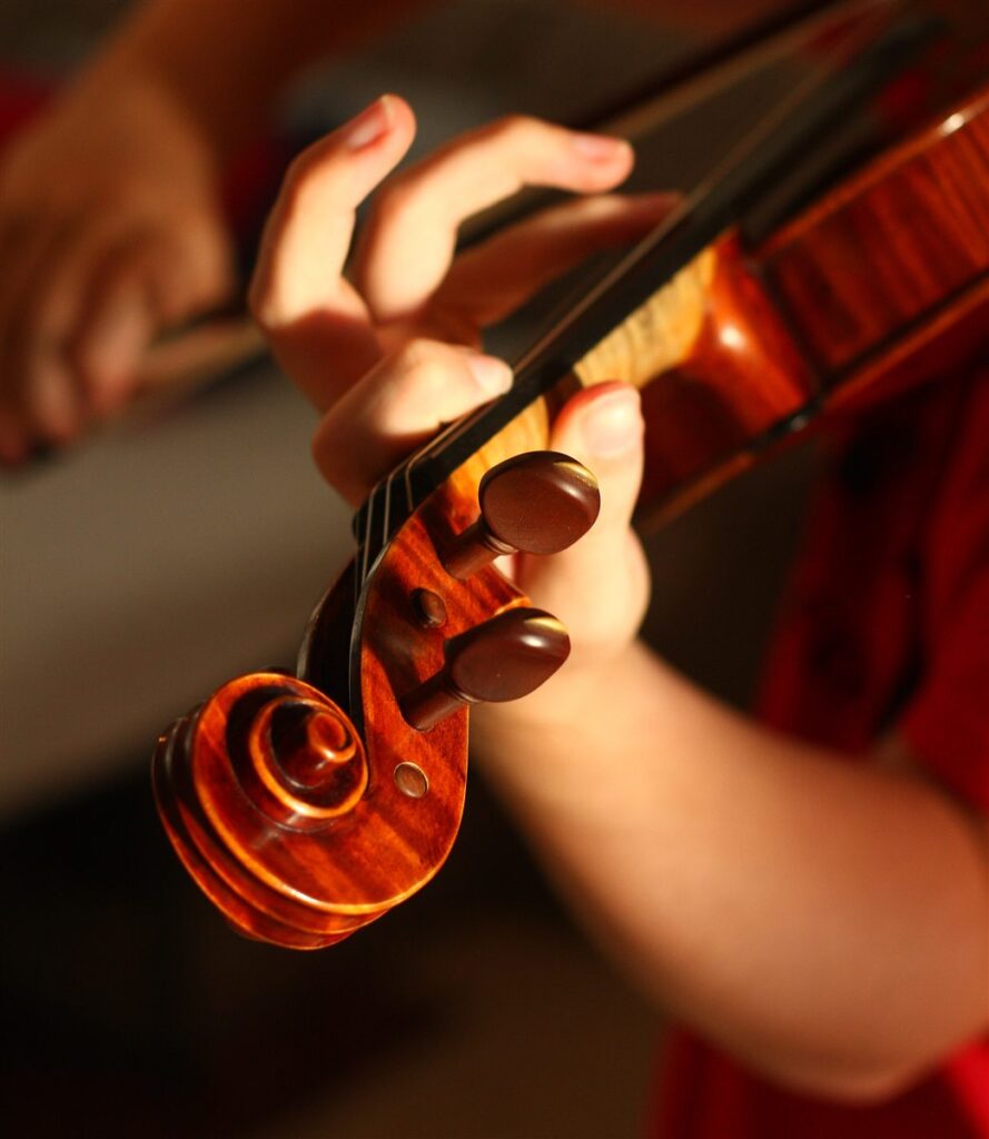 Voluta y clavijas de un viol&iacute;n mientras un m&uacute;sico pisa las cuerdas en el m&aacute;stil