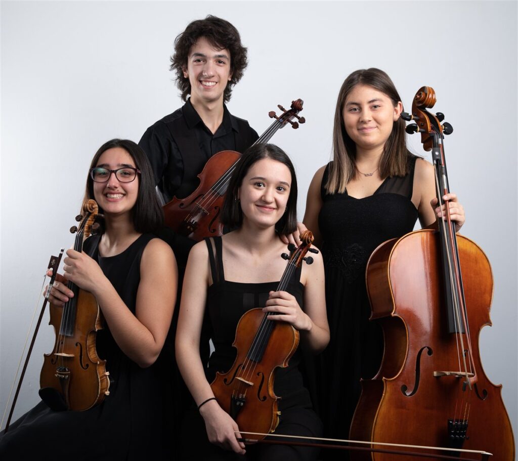 Cuatro jóvenes músicos posan con dos violines, una viola y un violonchelo, que muestran la diferencia de tamaño