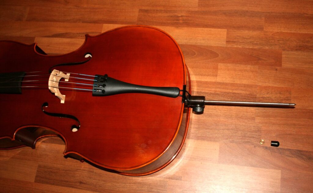 Pica metálica de un violonchelo con su tapón de goma, apoyada en un suelo de madera